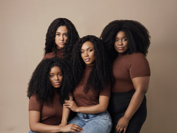 Quatro mulheres posando em um estúdio, usando camisetas marrons, apresentando diferentes estilos de cabelo naturalmente cacheado.
